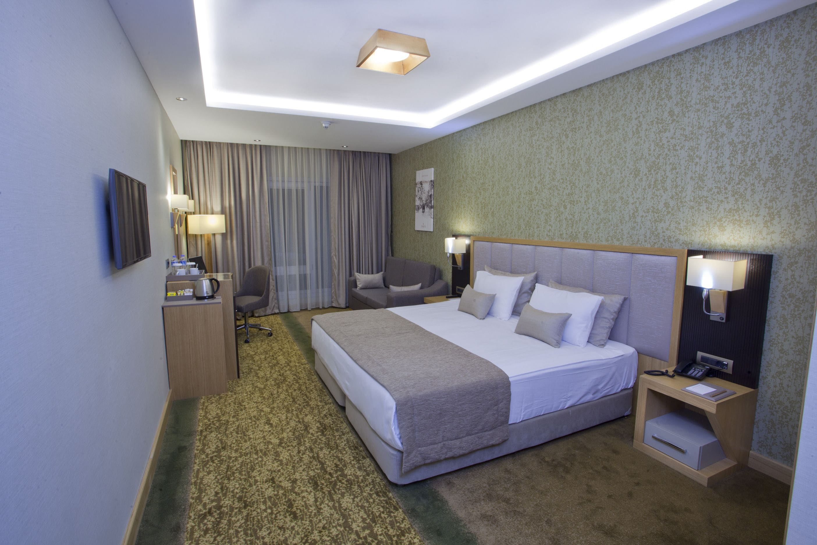 Ein Hotelzimmer mit einem großen Bett, einem Schreibtisch mit Stuhl, einem kleinen Tisch und einem Nachttisch mit Lampe.