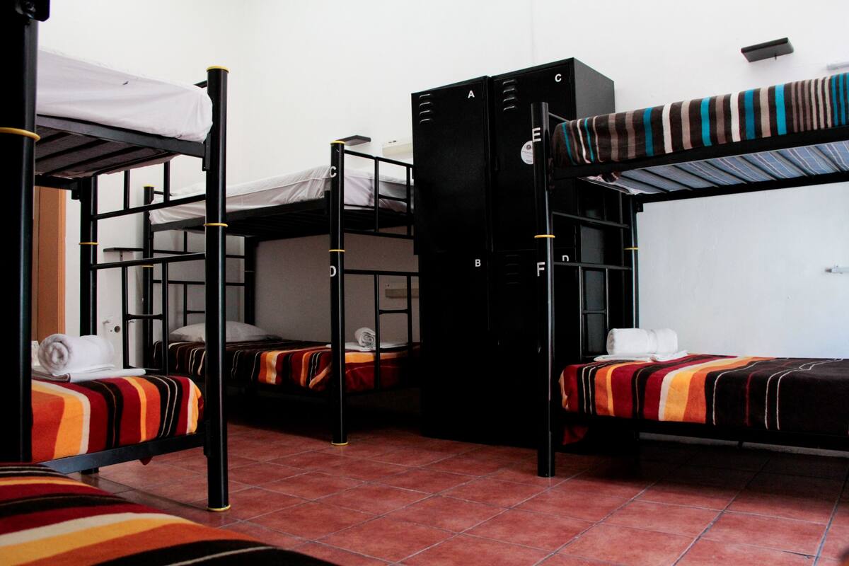 A dormitory room with bunk beds, a wardrobe, and a tiled floor.