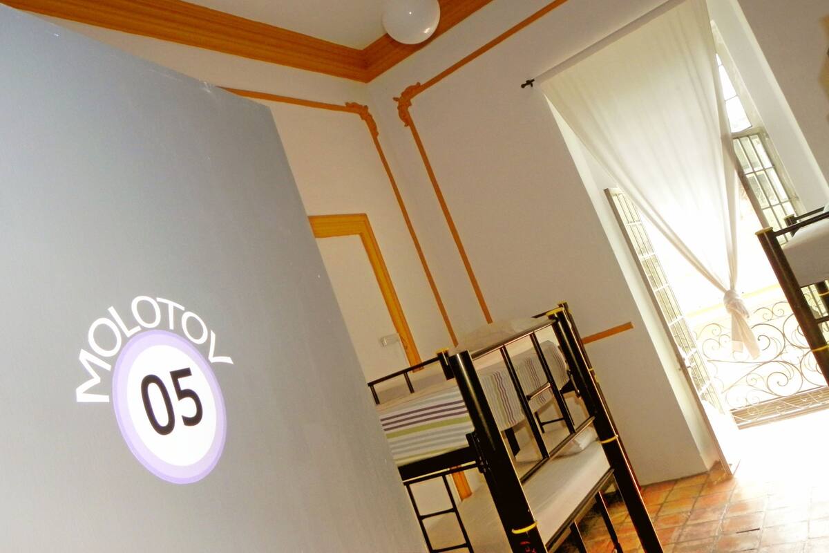 A room with a bunk bed, a sign with 'MOLOTON 05', and a window with curtains.