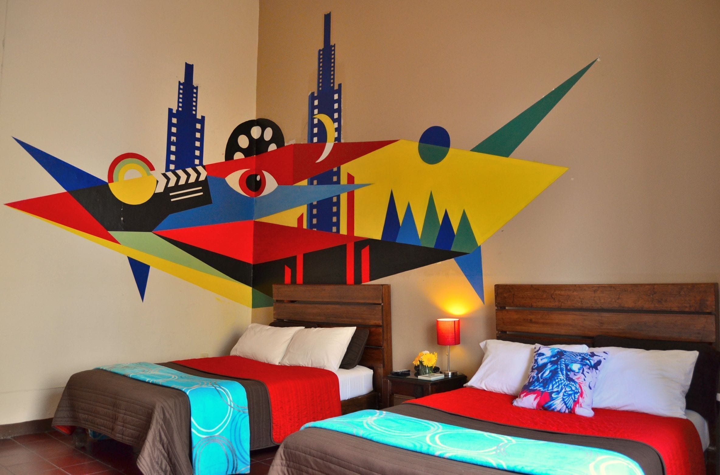 Une chambre d’hôtel avec deux lits, des têtes de lit en bois et une œuvre d’art murale abstraite aux couleurs vives.