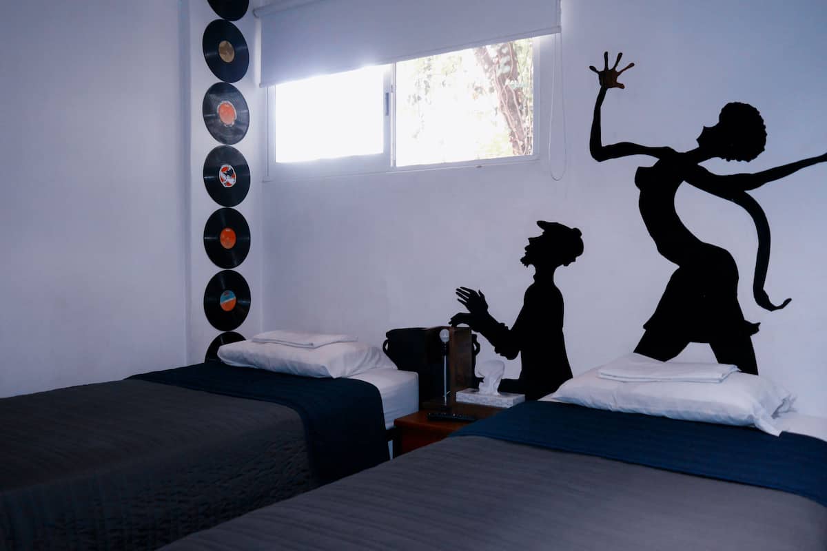 A room with two beds, a window, and a wall decorated with vinyl records and silhouettes.
