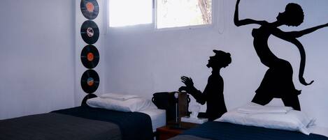 Une chambre avec deux lits, une fenêtre et un mur décoré de disques vinyles et de silhouettes.