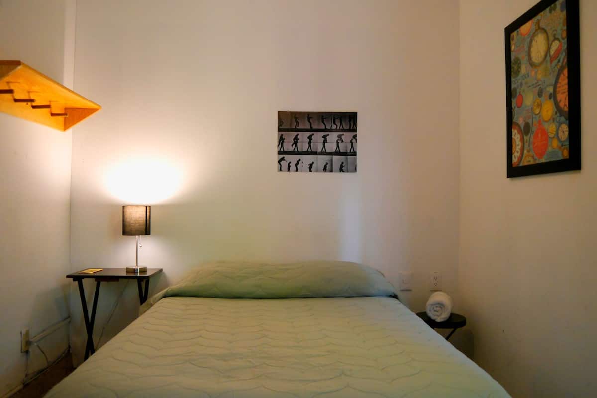 A bedroom with a bed, a nightstand, a wall-mounted lamp, and a framed picture.