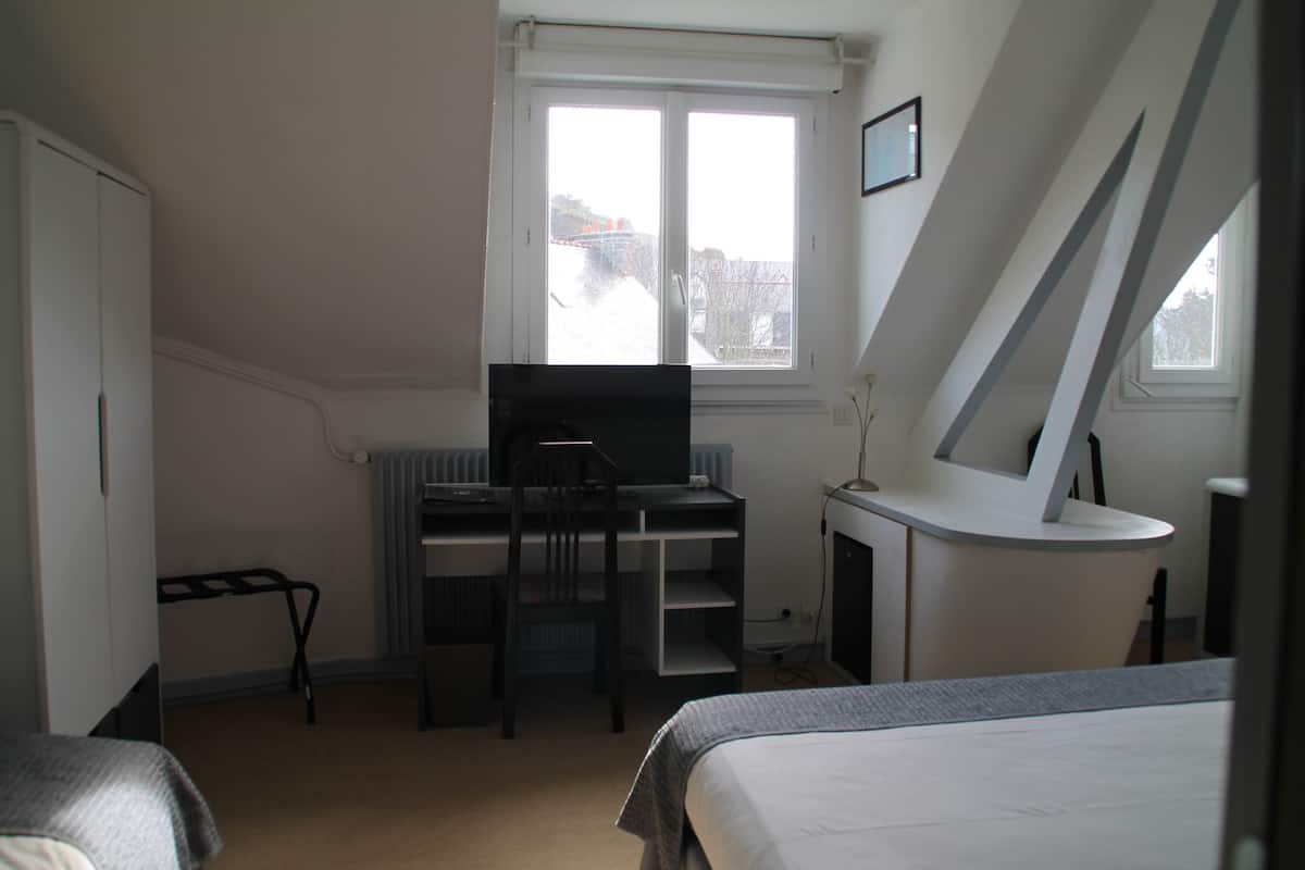 A bedroom with a bed, a desk, a chair, a radiator, and a window.