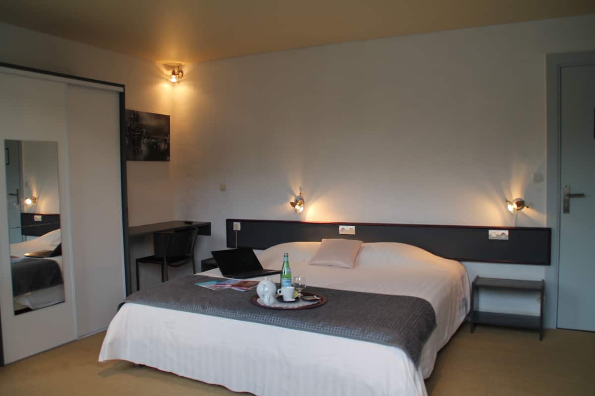 A hotel room with a bed, bedside table, chair, and a desk with a laptop.