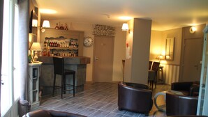 A bar area with a counter and stools, a clock on the wall, and a seating area with chairs. - Hotel de la Mer (Pleneuf-Val-Andre)