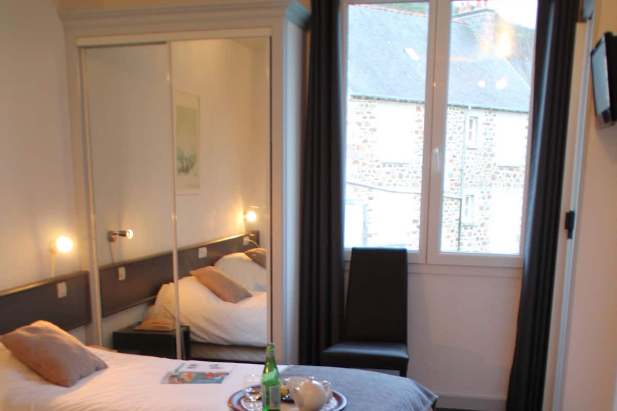 A hotel room with two beds, a mirror, a window with curtains, and a small table with a bottle and a tray.
