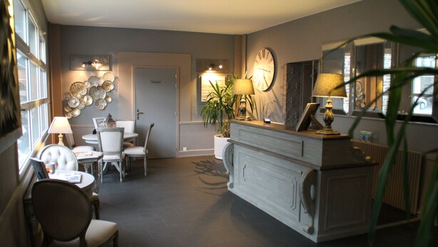A dining area with a table and chairs, a bar area with a counter and a clock, and a door leading to another room. - Hotel de la Mer (Pleneuf-Val-Andre)