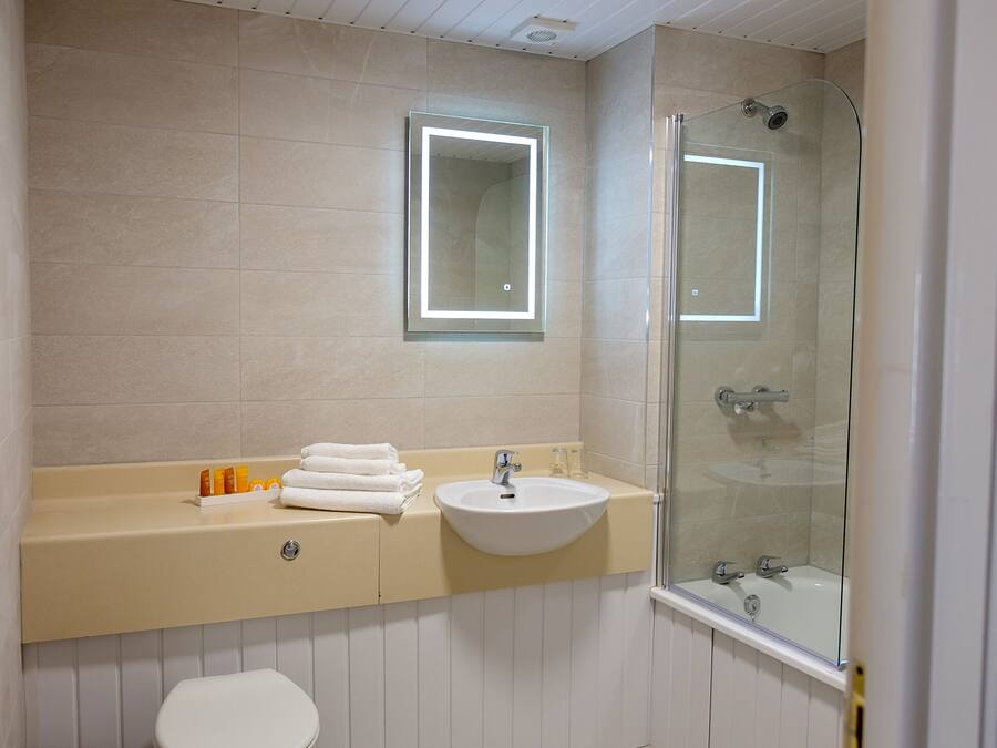 Un baño con inodoro, lavamanos y ducha con mampara de vidrio.