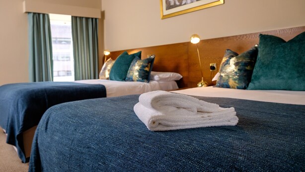 A hotel room with two beds, each with a blue bedspread and a white towel on the bed. There is a framed picture on the wall above the beds. - Charlemont Arms Hotel (Armagh)