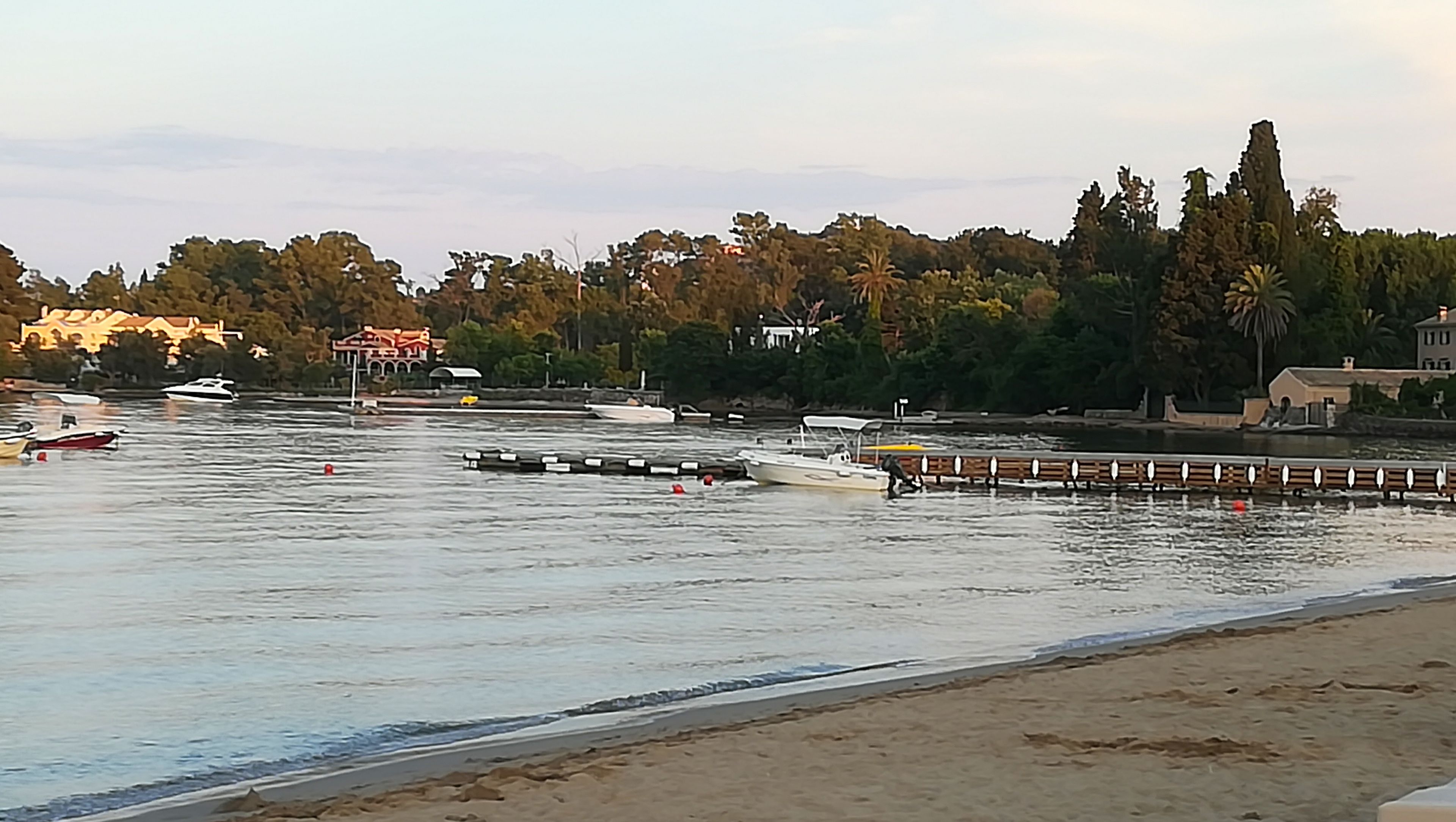 Escena costera con barcos, un muelle y edificios al fondo.