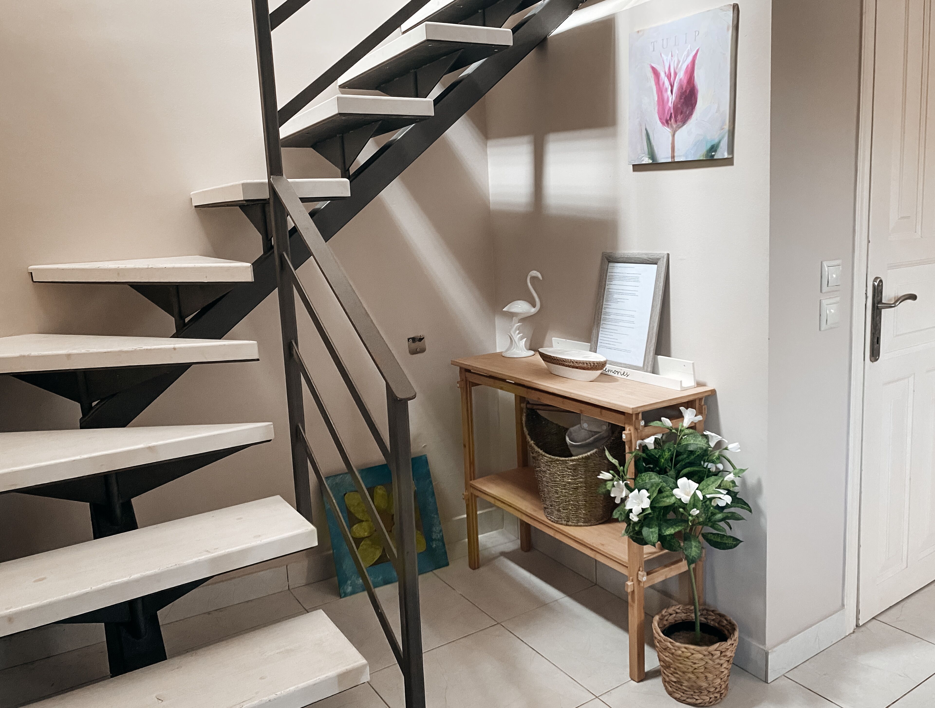 A staircase with a black metal railing, a wooden table with baskets, and a framed picture on the wall.