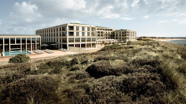 A modern hotel with multiple floors, a swimming pool, and a beach view.