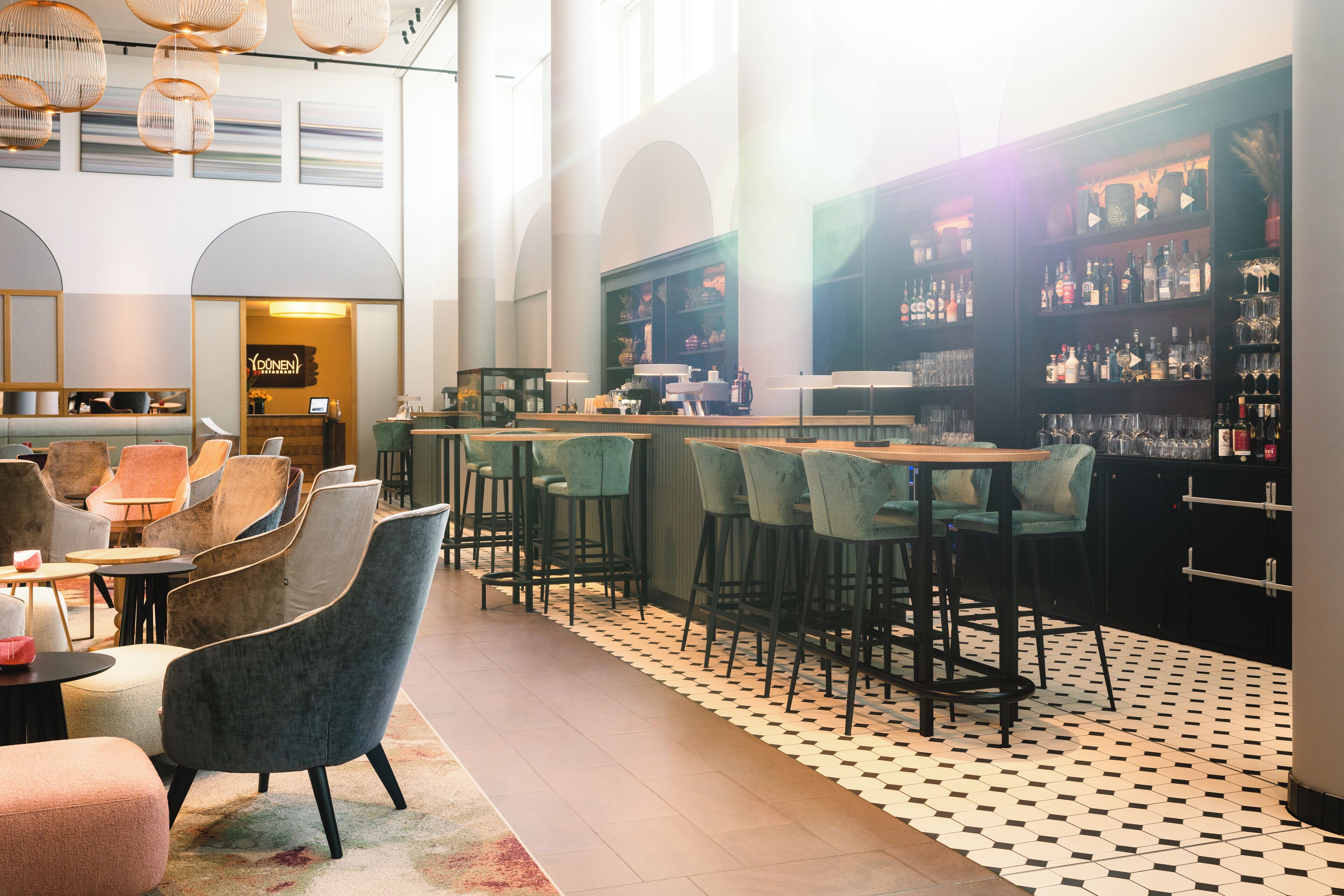 A modern bar area with high ceilings, bar stools, and a variety of liquor bottles.
