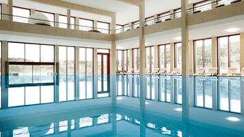 A large indoor swimming pool with multiple levels and sunlit windows.