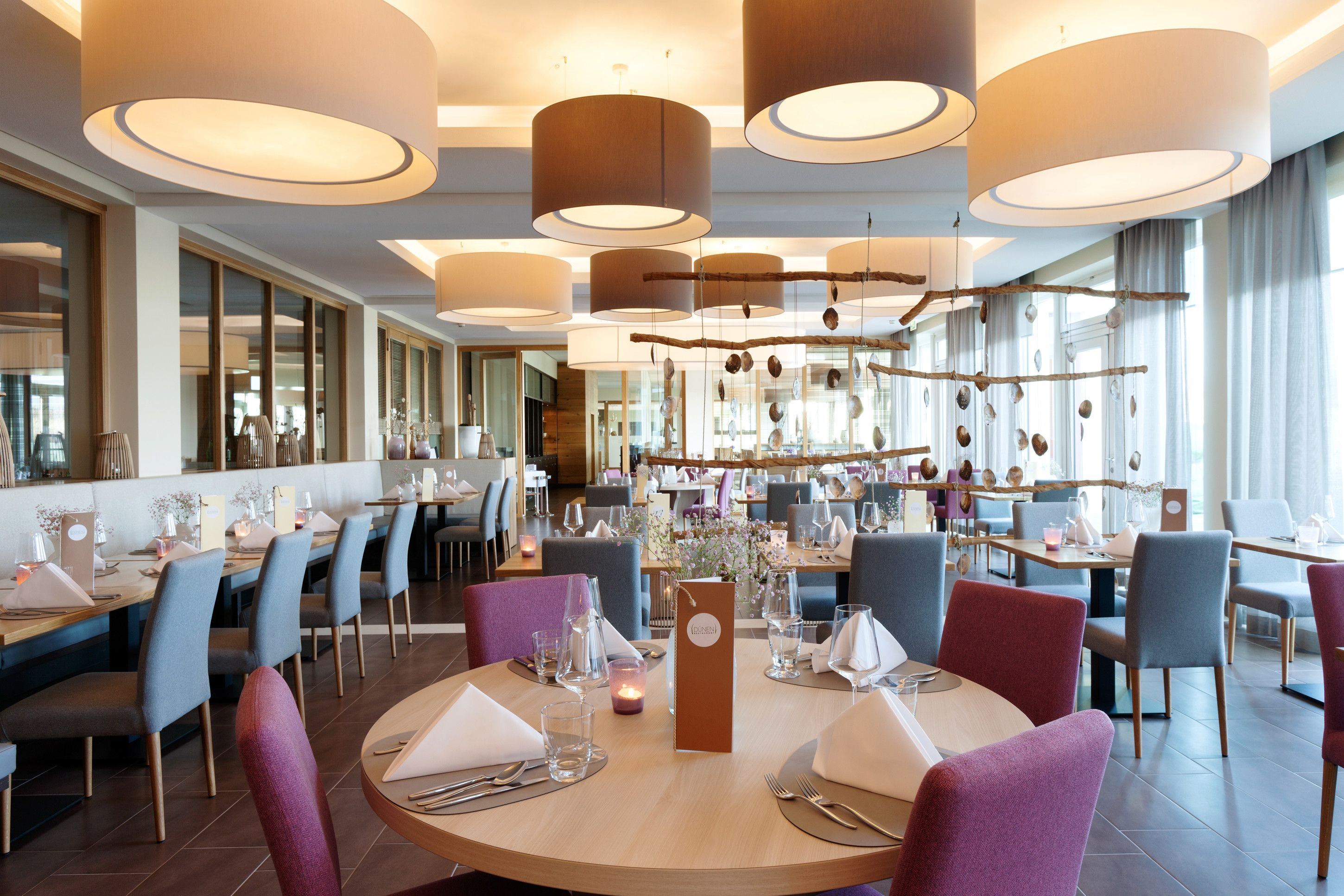 A modern restaurant with round tables, blue and purple chairs, and pendant lighting.