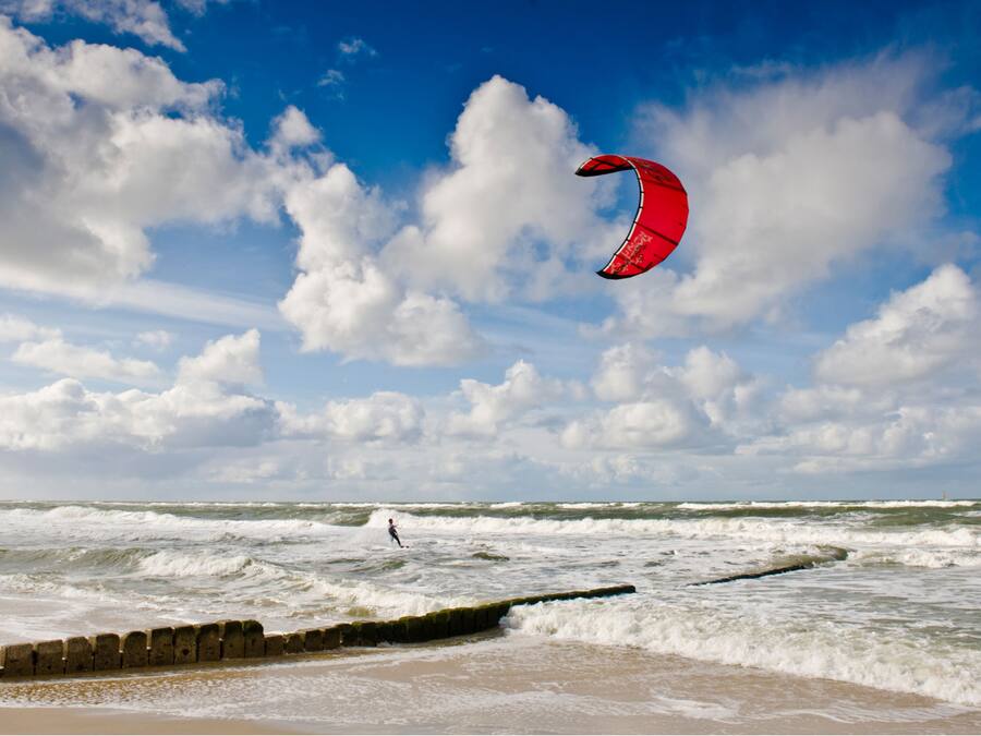 A beach with waves and a person kite surfing.