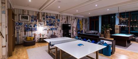 A modern indoor space with a ping pong table, pool table, and various sports equipment.