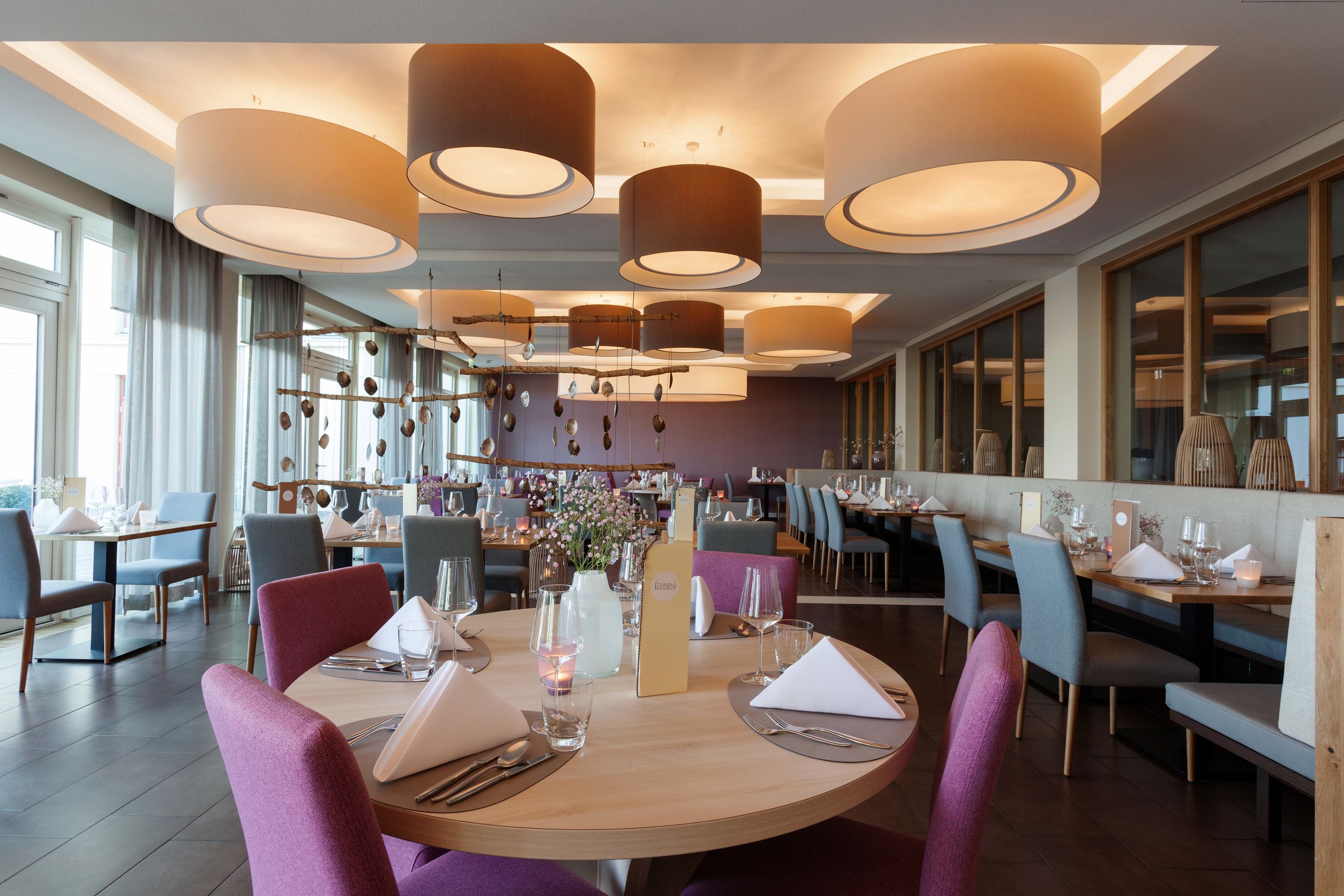 A restaurant with round tables, purple chairs, and hanging pendant lights.