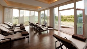 A spa room with multiple sun loungers, large windows, and a wooden ceiling.