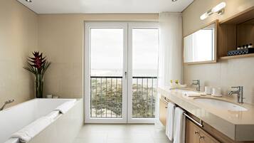 Ein modernes Badezimmer mit Badewanne, großem Spiegel, Waschtisch und Blick auf den Strand durch eine Glastür.