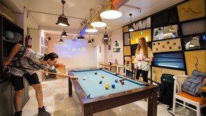 Une table de billard dans une pièce équipée d’un écran de projection, d’un ventilateur et d’étagères remplies de divers objets.