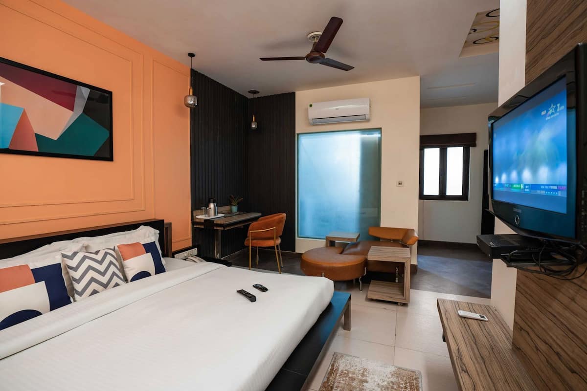 A hotel room with a bed, a desk, a chair, a television, and an air conditioning unit.