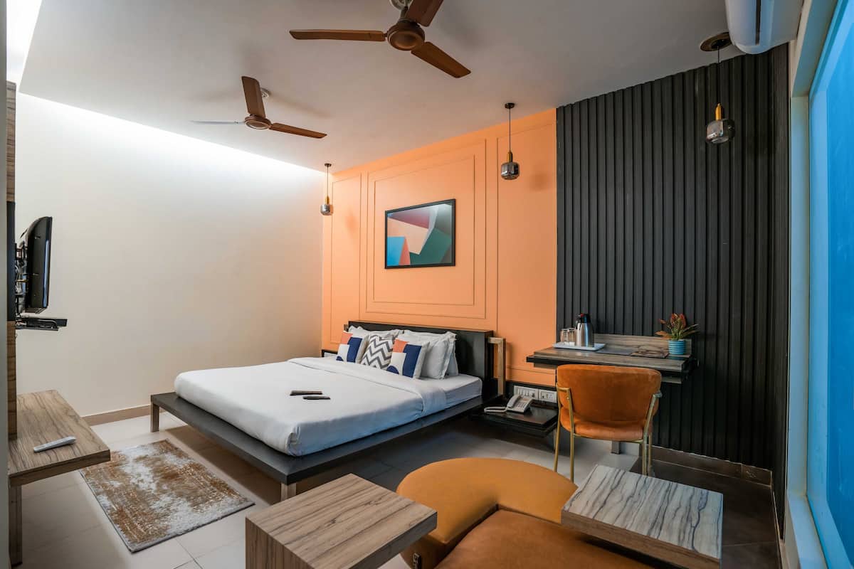 A modern hotel room with a bed, desk, chair, and ceiling fans.