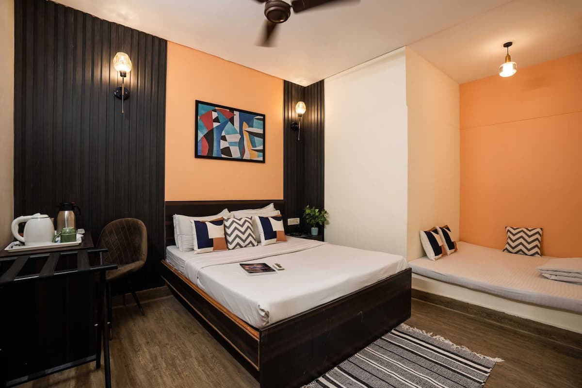 A modern hotel room with a bed, bedside table, chair, and a small seating area with cushions.