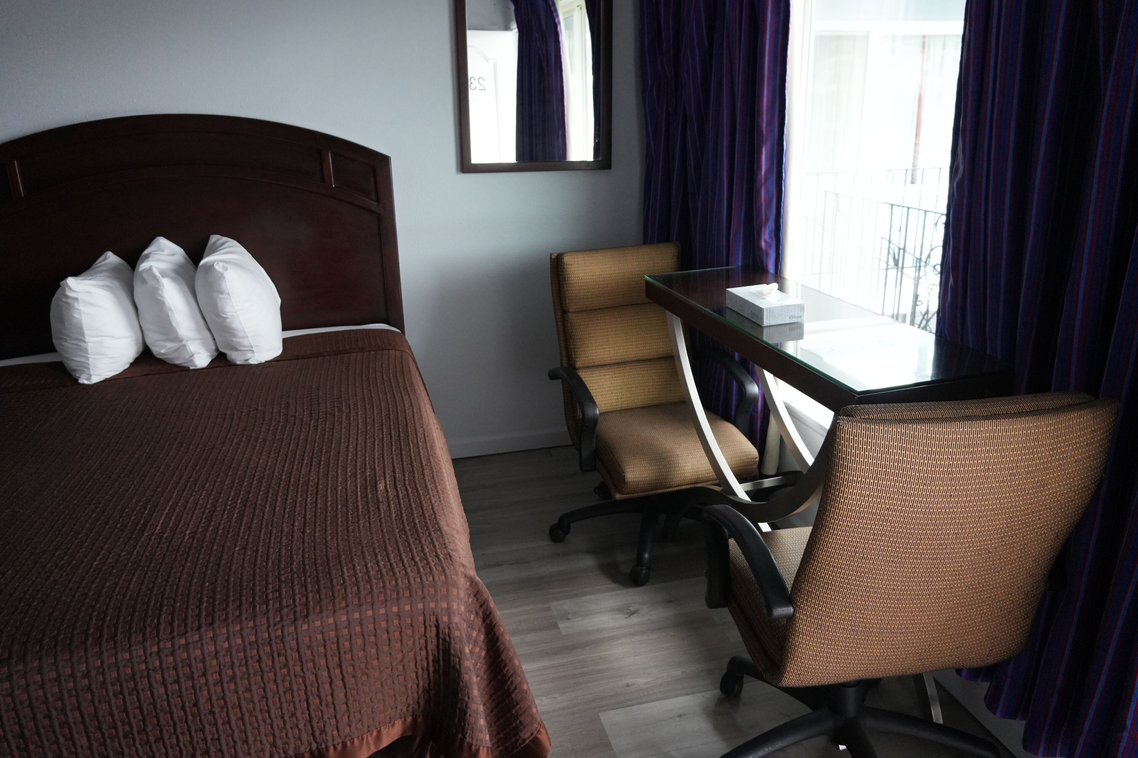 Una habitación de hotel con cama, escritorio, silla y ventana con cortinas.