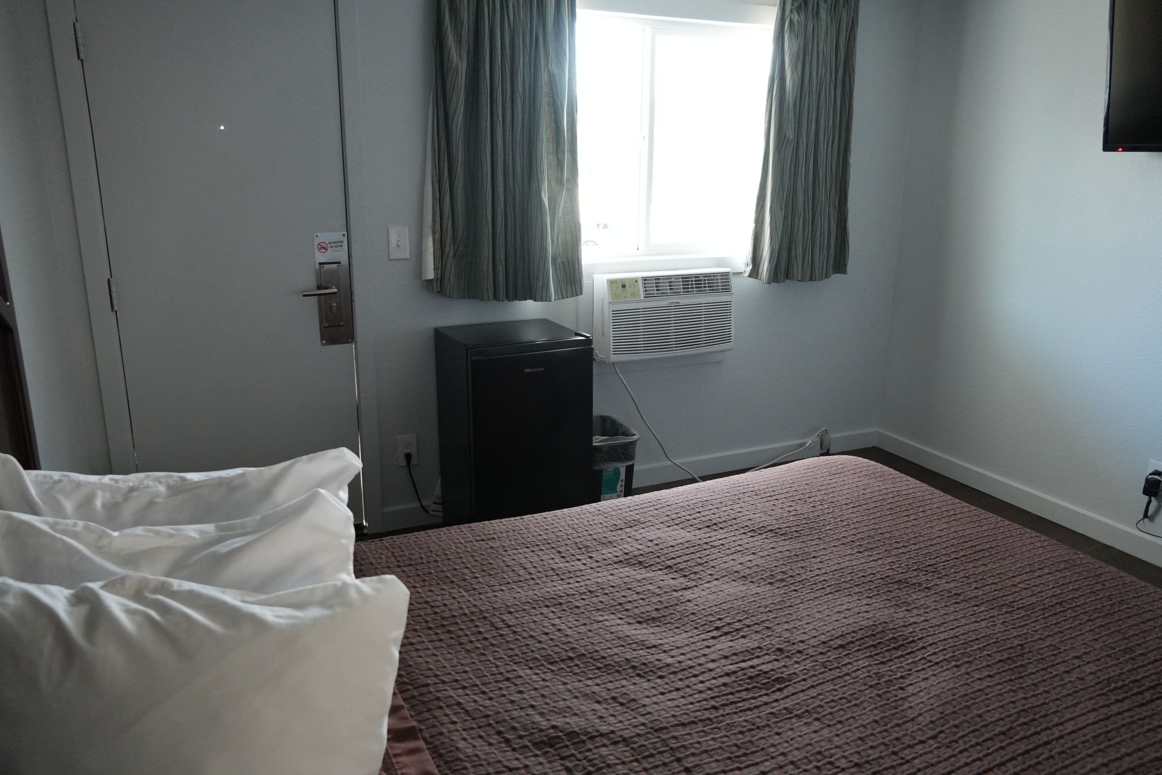 Ein Hotelzimmer mit Bett, Schreibtisch, Klimaanlage und einem Fenster mit Vorhängen.