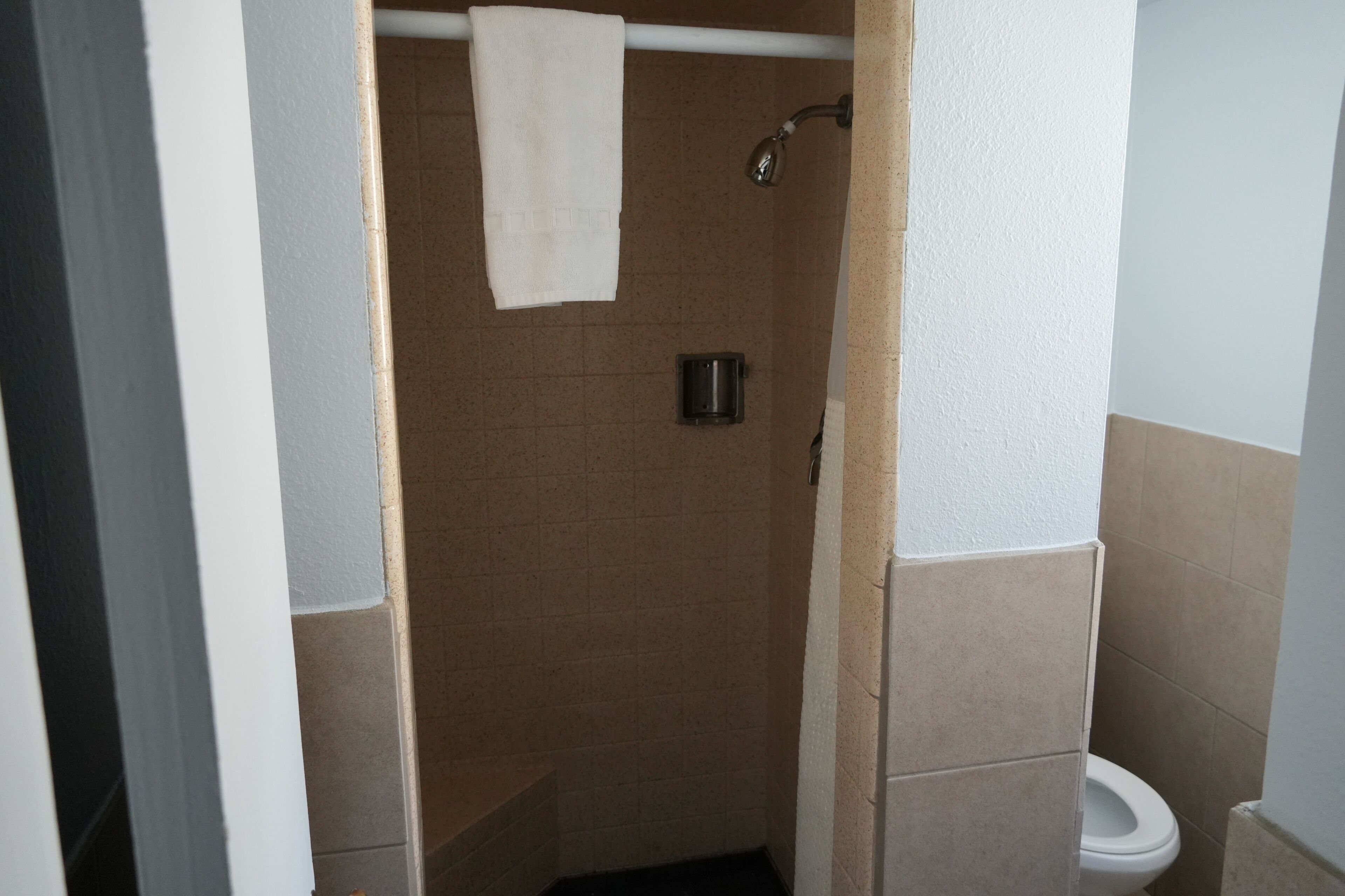 A bathroom with a shower, a toilet, and a towel hanging on a rod.