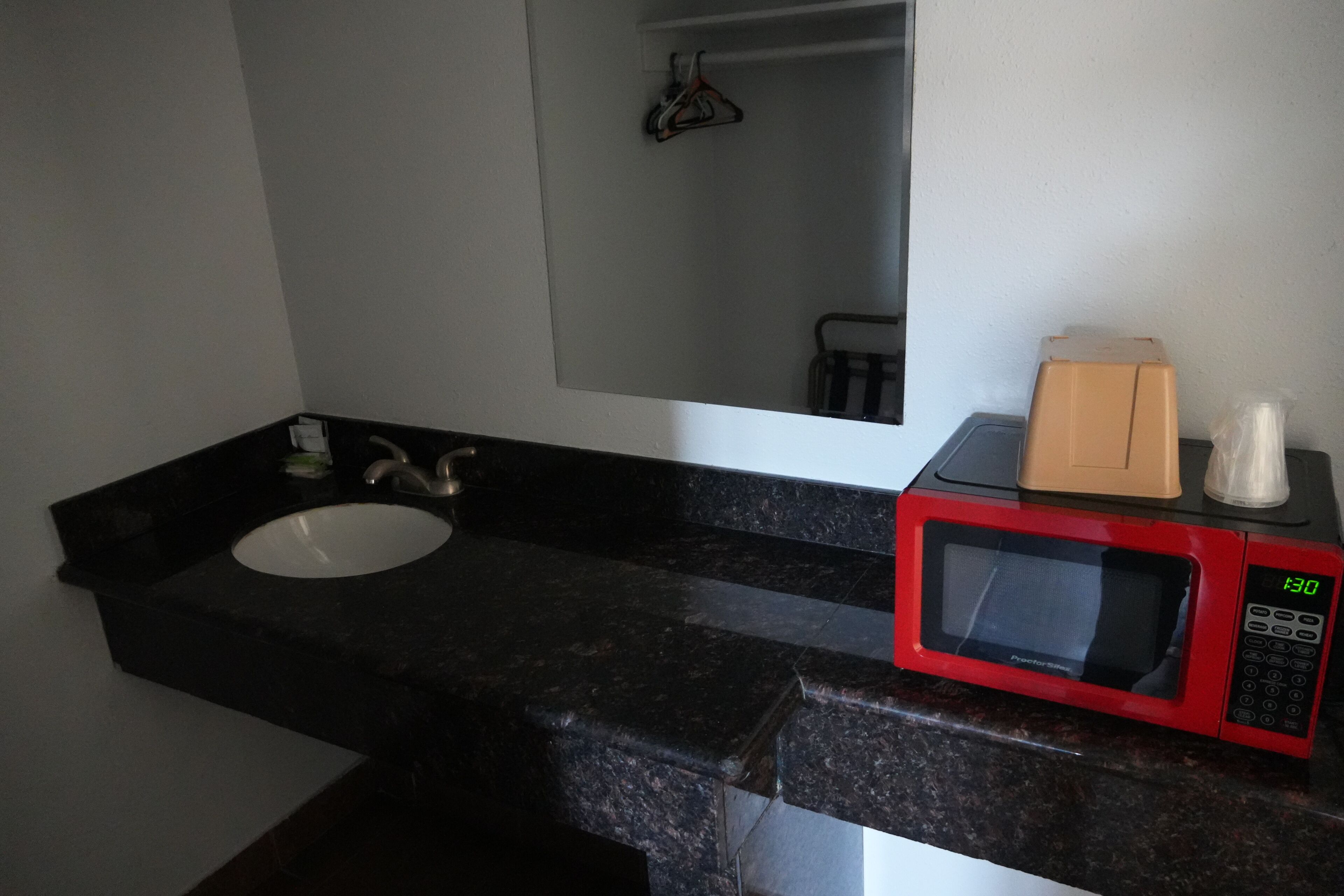 Un baño con encimera de granito negro, un lavabo blanco, un microondas rojo y un espejo sobre el lavabo.