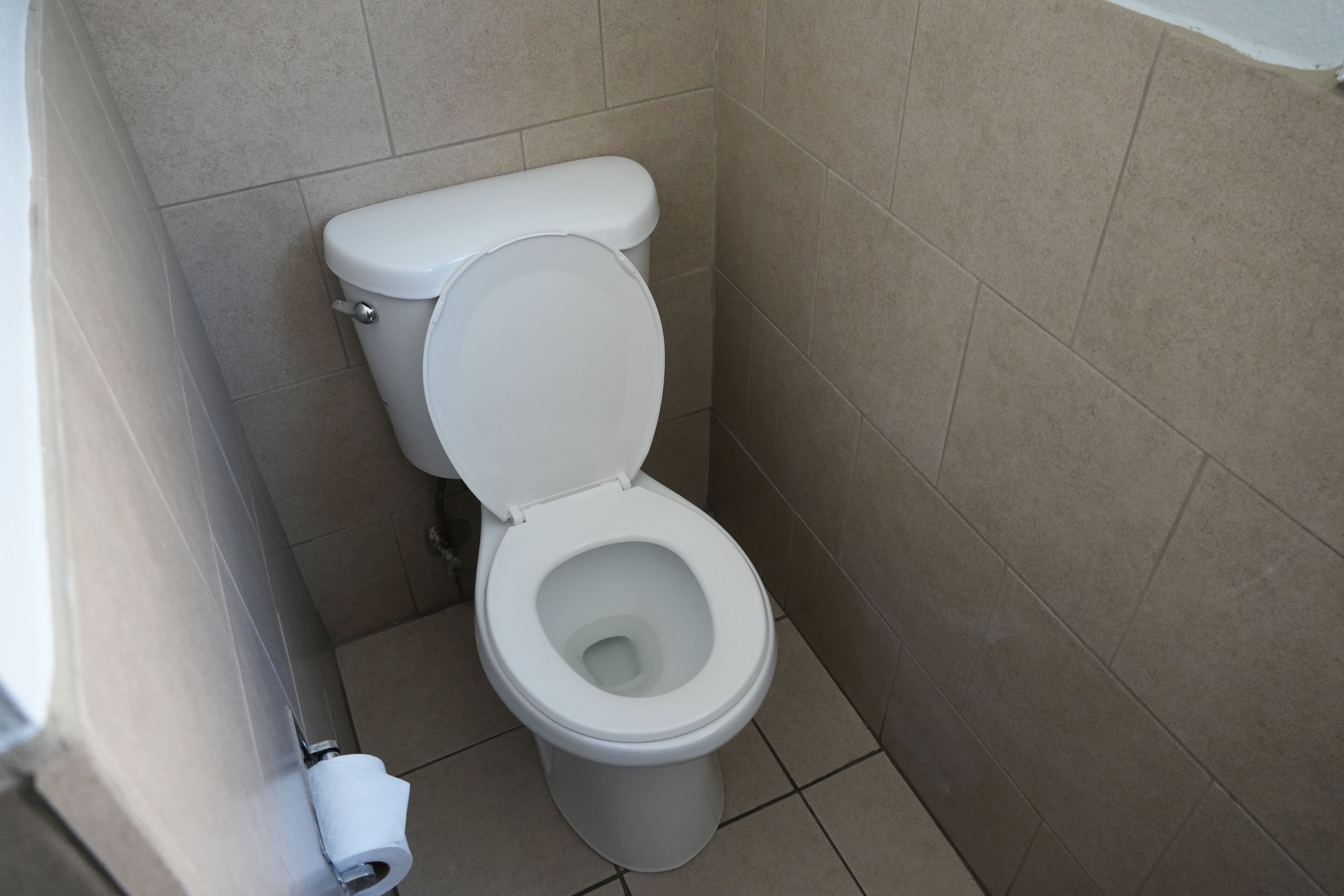 Un inodoro blanco en un baño con azulejos color beige.