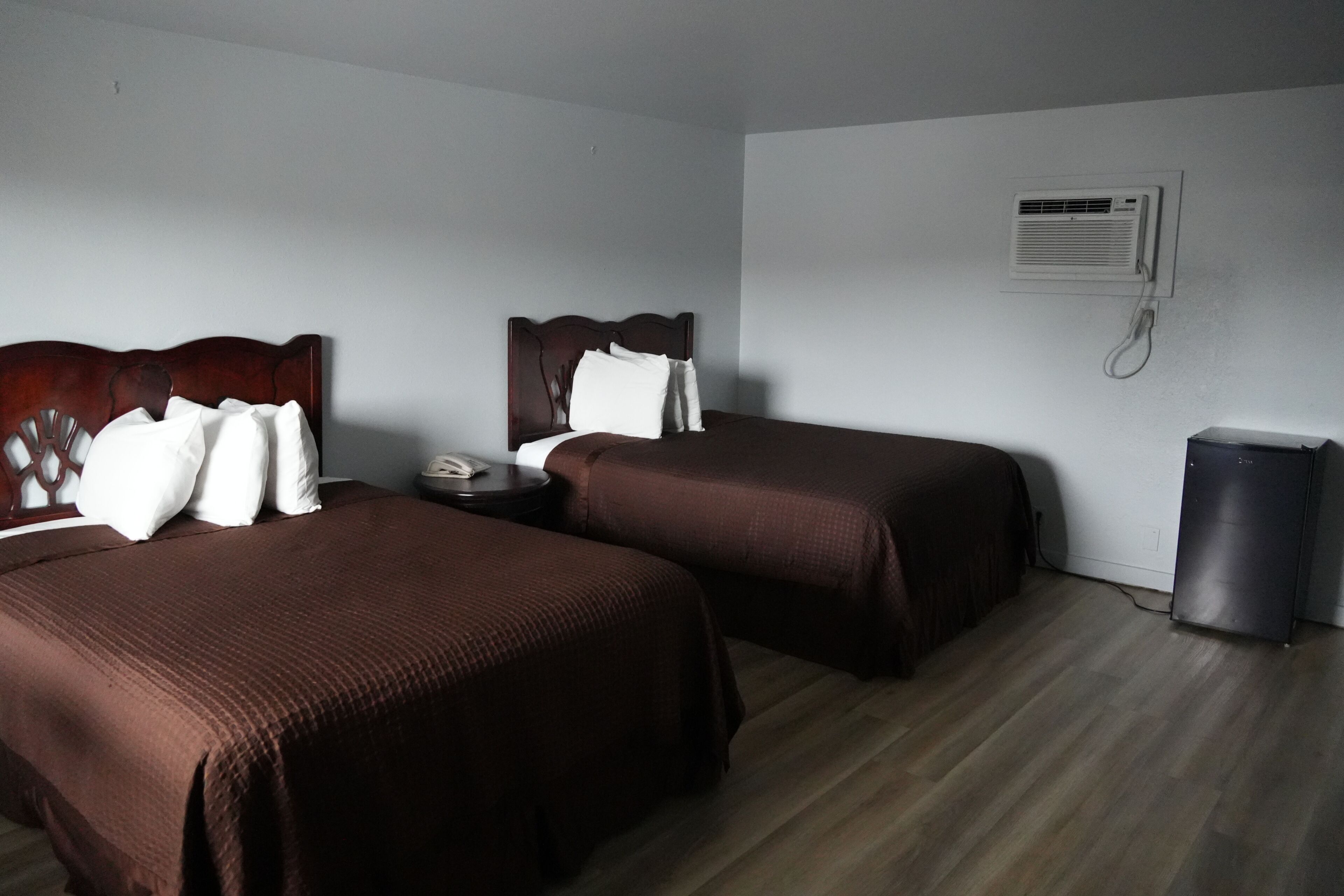 Ein Hotelzimmer mit zwei Betten, einem Nachttisch, einem Telefon, einer Klimaanlage und einem Mülleimer.