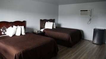 Ein Hotelzimmer mit zwei Betten, einem Nachttisch, einem Telefon, einer Klimaanlage und einem Mülleimer.