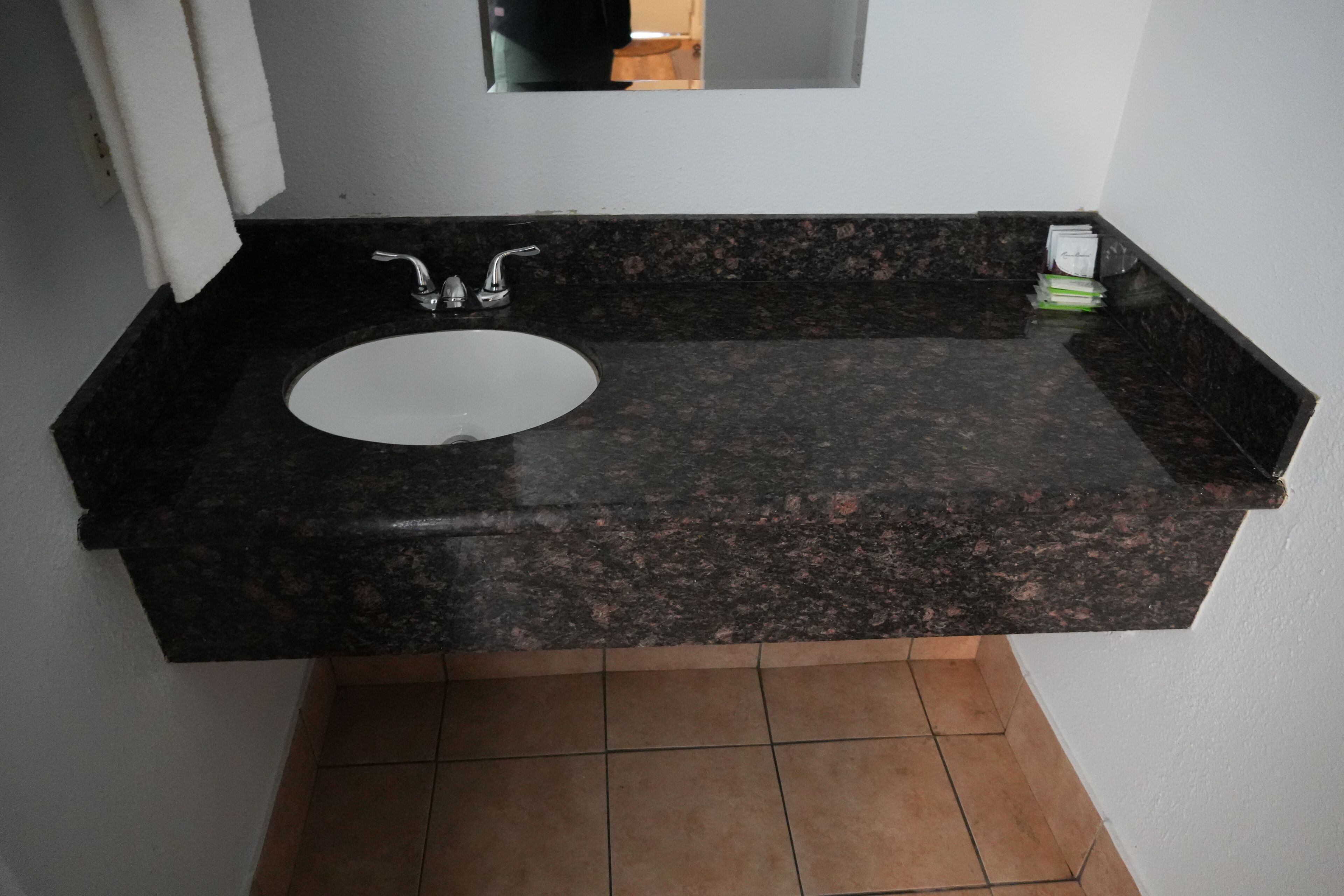 Un bagno con lavandino bianco, piano di lavoro in granito scuro e specchio sopra.
