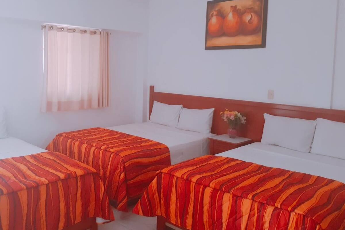 Een hotelkamer met twee enkele bedden, een houten hoofdbord, een nachtkastje met een bloevas en een schilderij aan de muur.