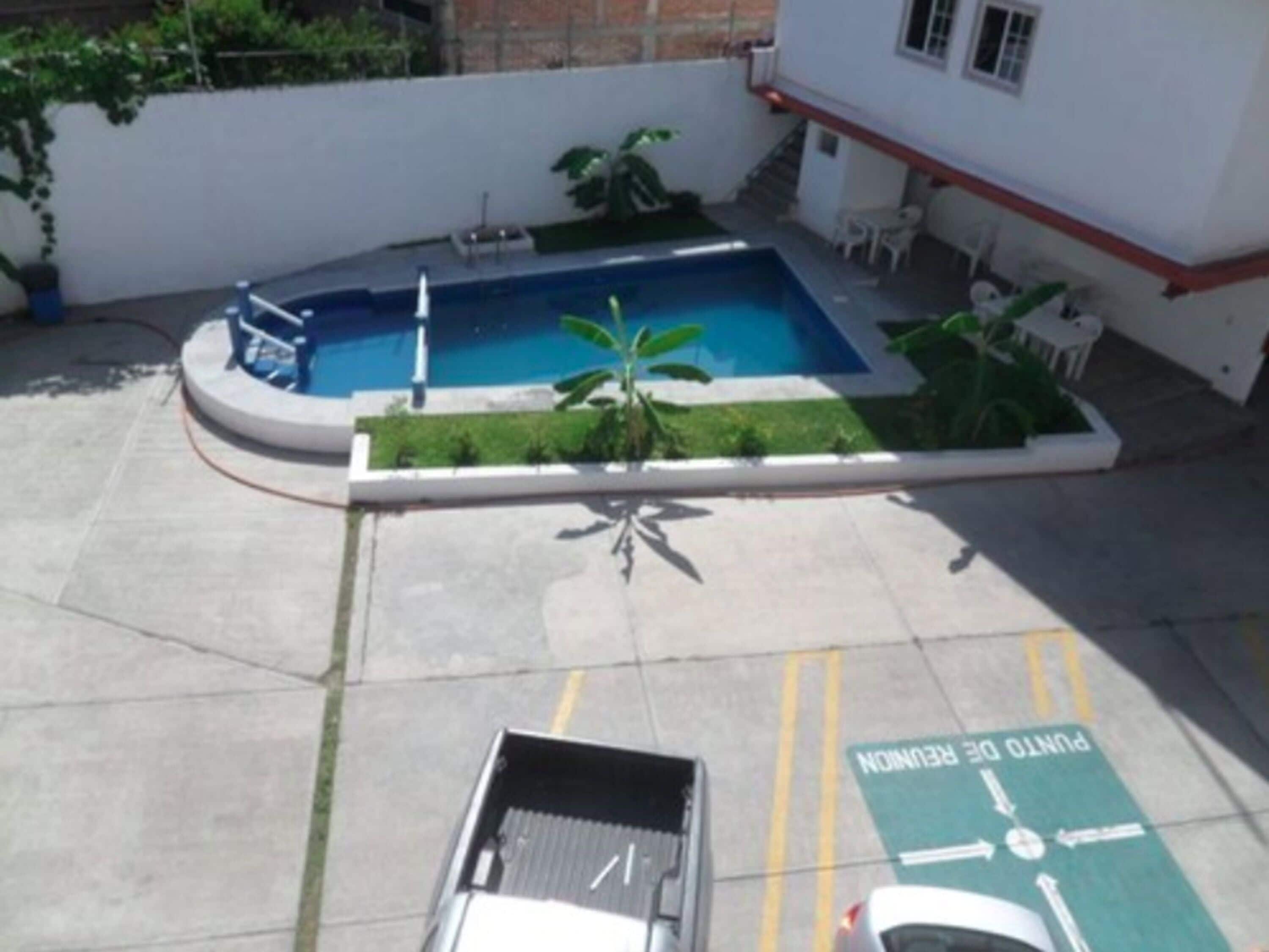 A swimming pool with a small garden area, a covered seating area, and a parking space marked with directional arrows.