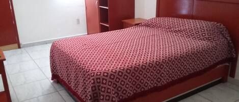 A single-bed room with a patterned bedspread, a wooden headboard, a nightstand, and a wardrobe.
