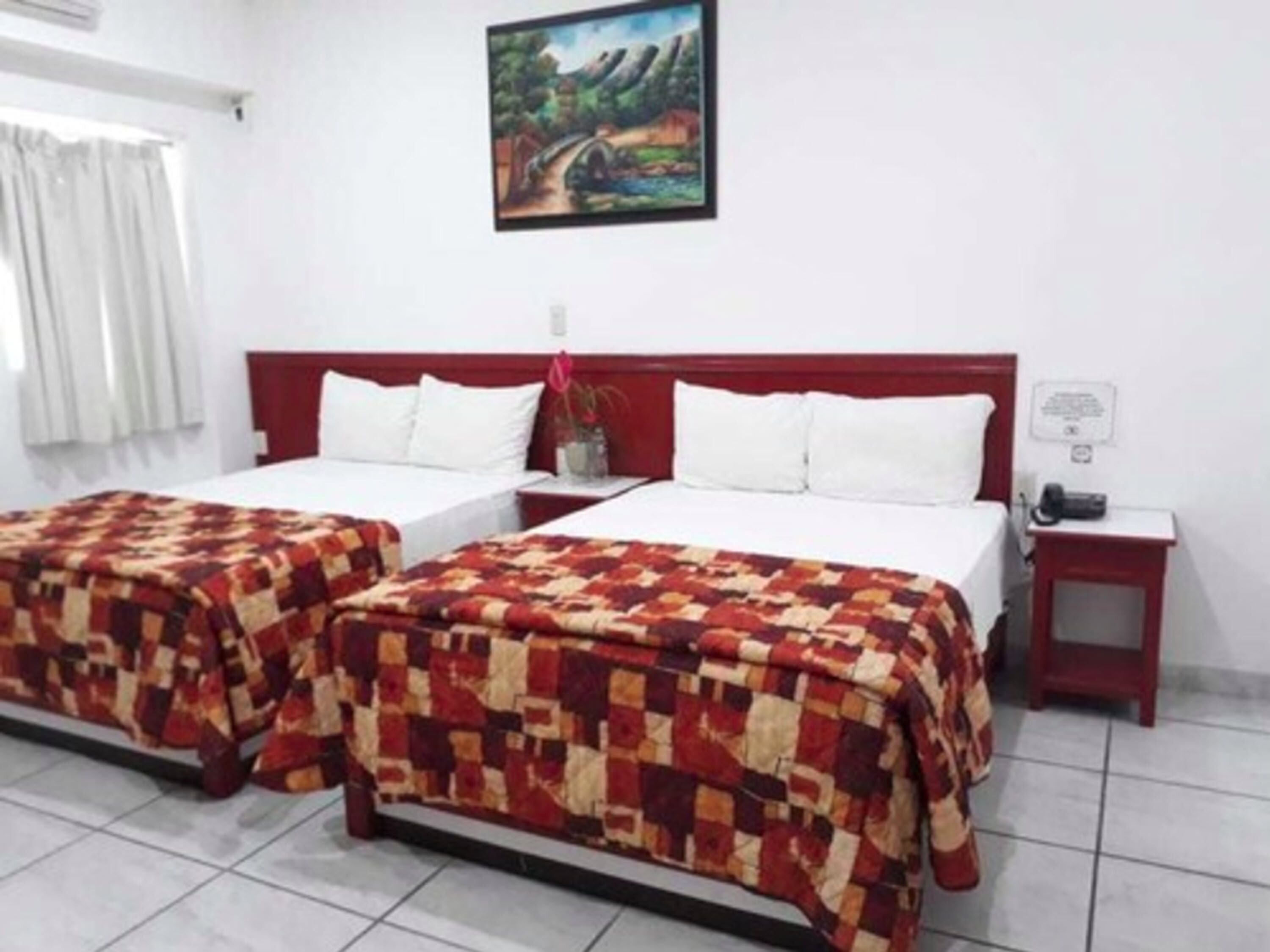 A hotel room with two beds, a painting on the wall, and a telephone on the nightstand.