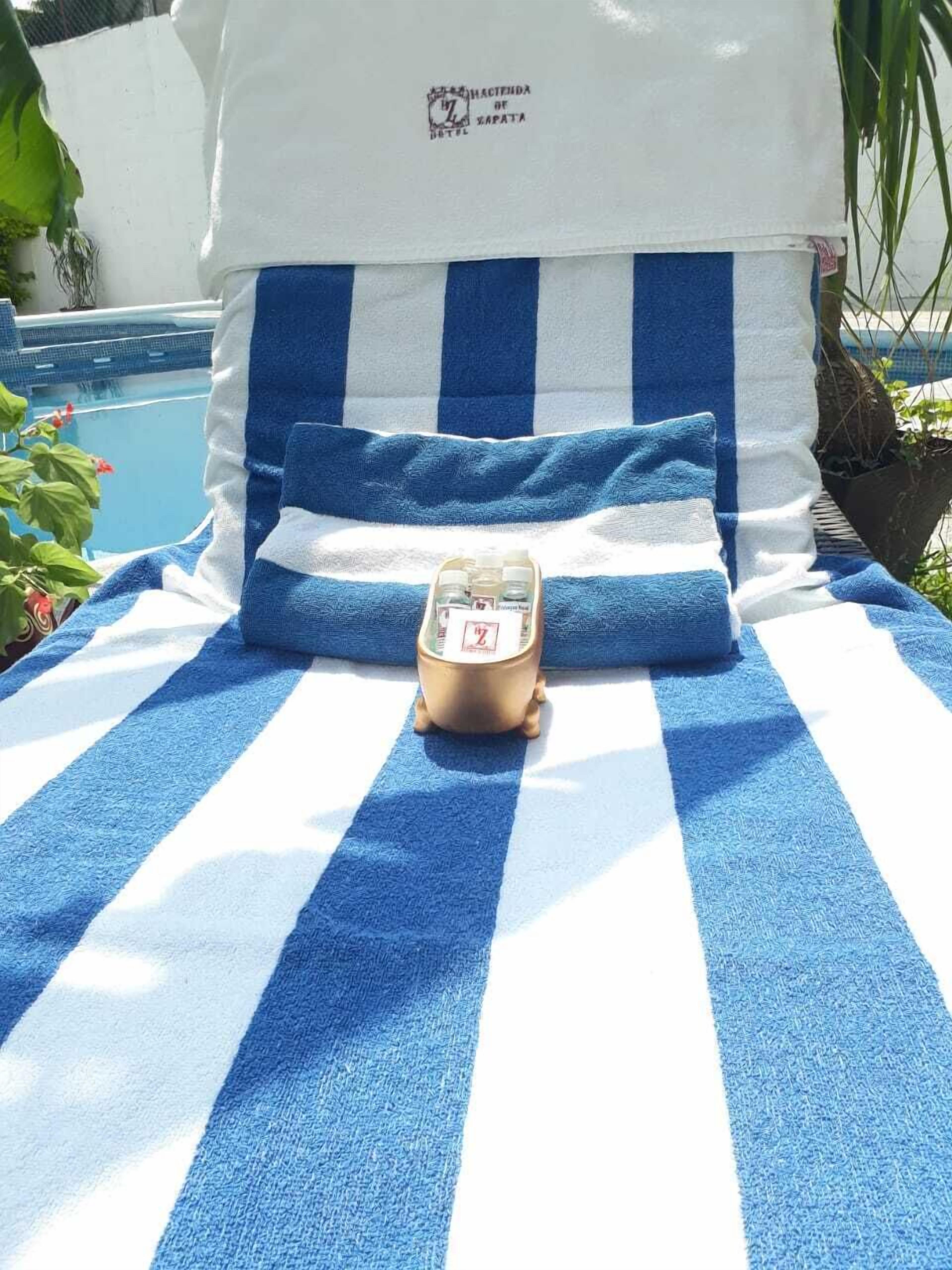 A bed with a blue and white striped towel, a small golden clock, and a pillow with a logo.