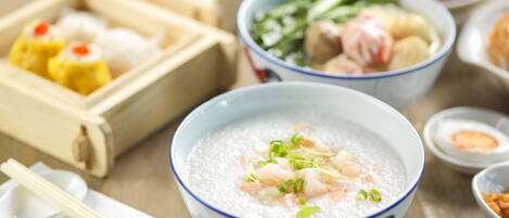 Une variété de plats asiatiques, notamment un bol de soupe aux crevettes et aux légumes, ainsi que plusieurs autres plats servis dans des boîtes en bois.