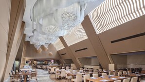 Un hall de hotel espacioso con varias zonas de comedor, un atrio central y un candelabro moderno.