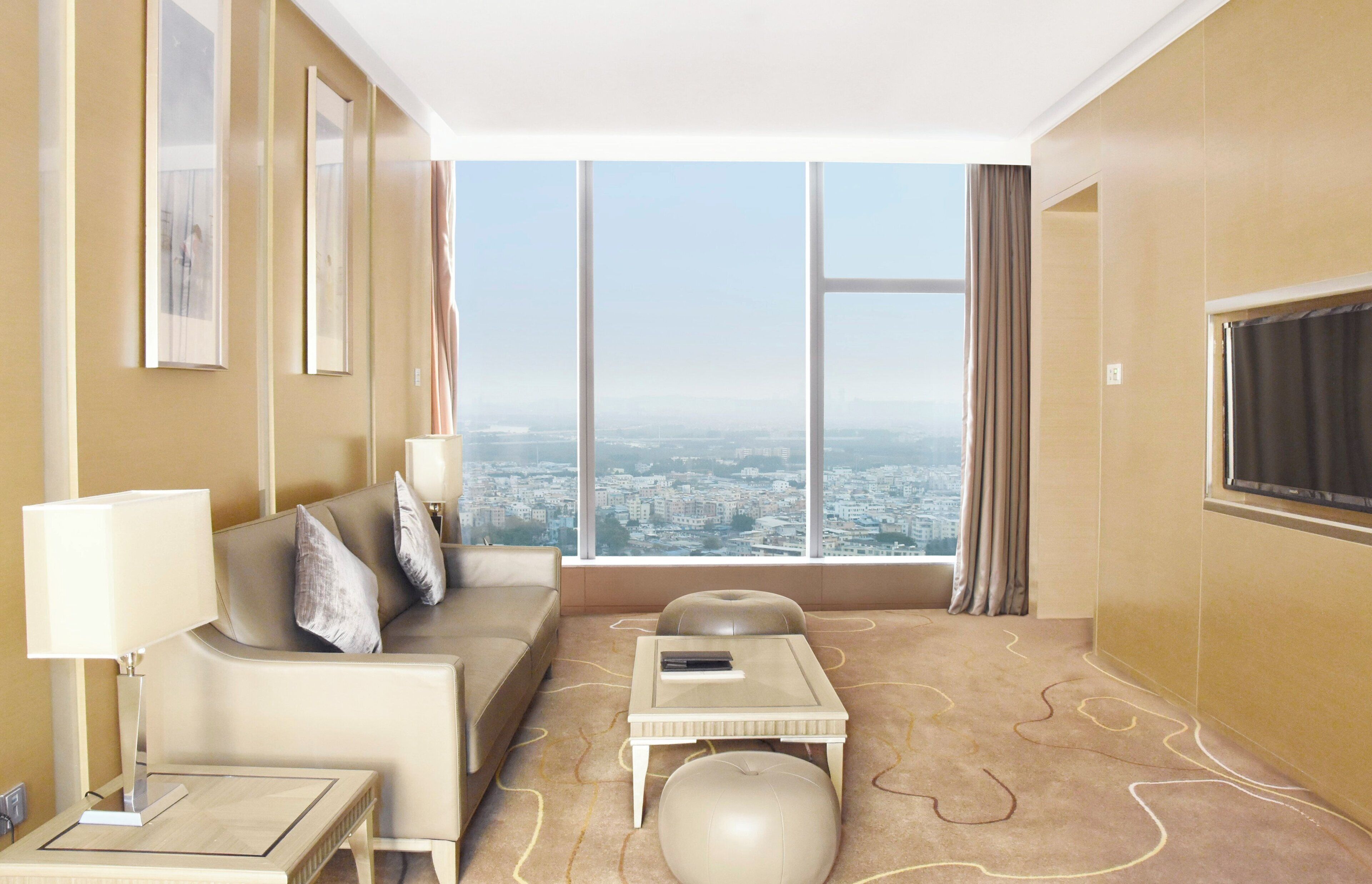 Habitación de hotel moderna con un ventanal grande que ofrece vista a la ciudad, un sofá, una mesita y una lámpara.