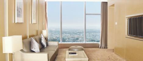 Habitación de hotel moderna con un ventanal grande que ofrece vista a la ciudad, un sofá, una mesita y una lámpara.