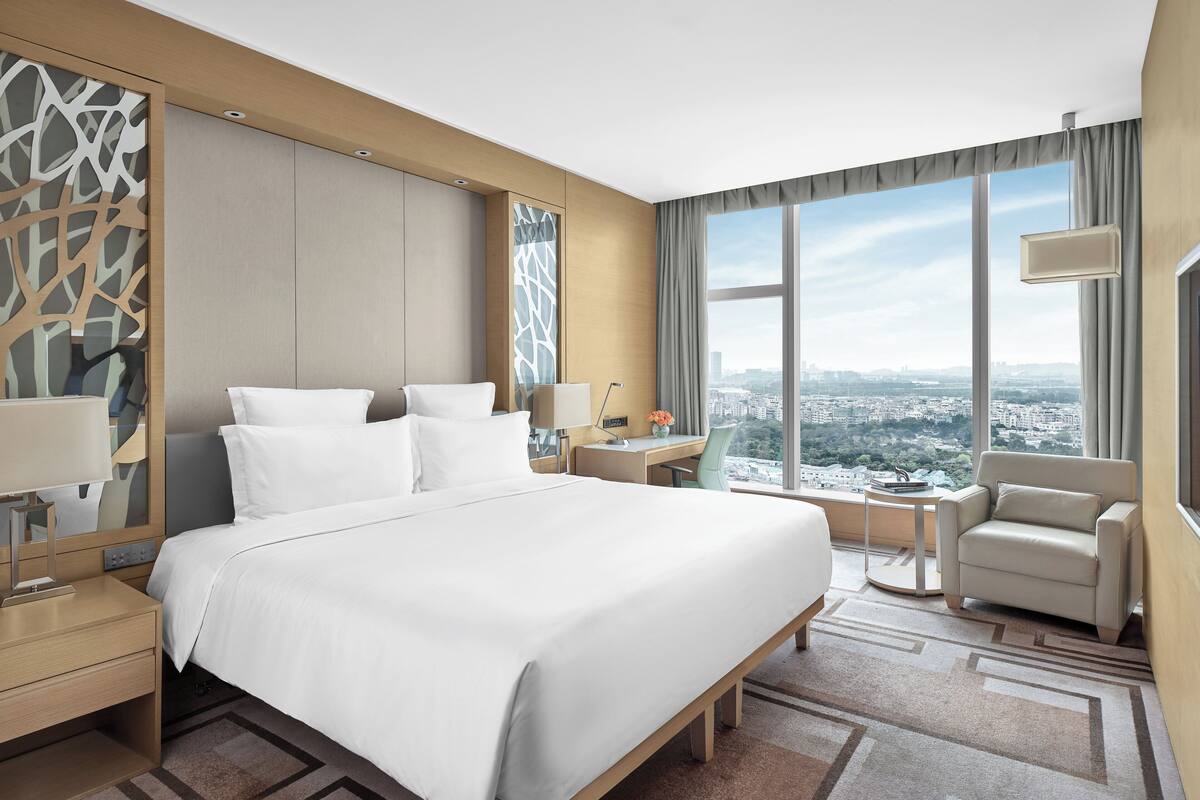 Habitación de hotel moderna con una cama grande, un escritorio, una silla y vistas a la ciudad.