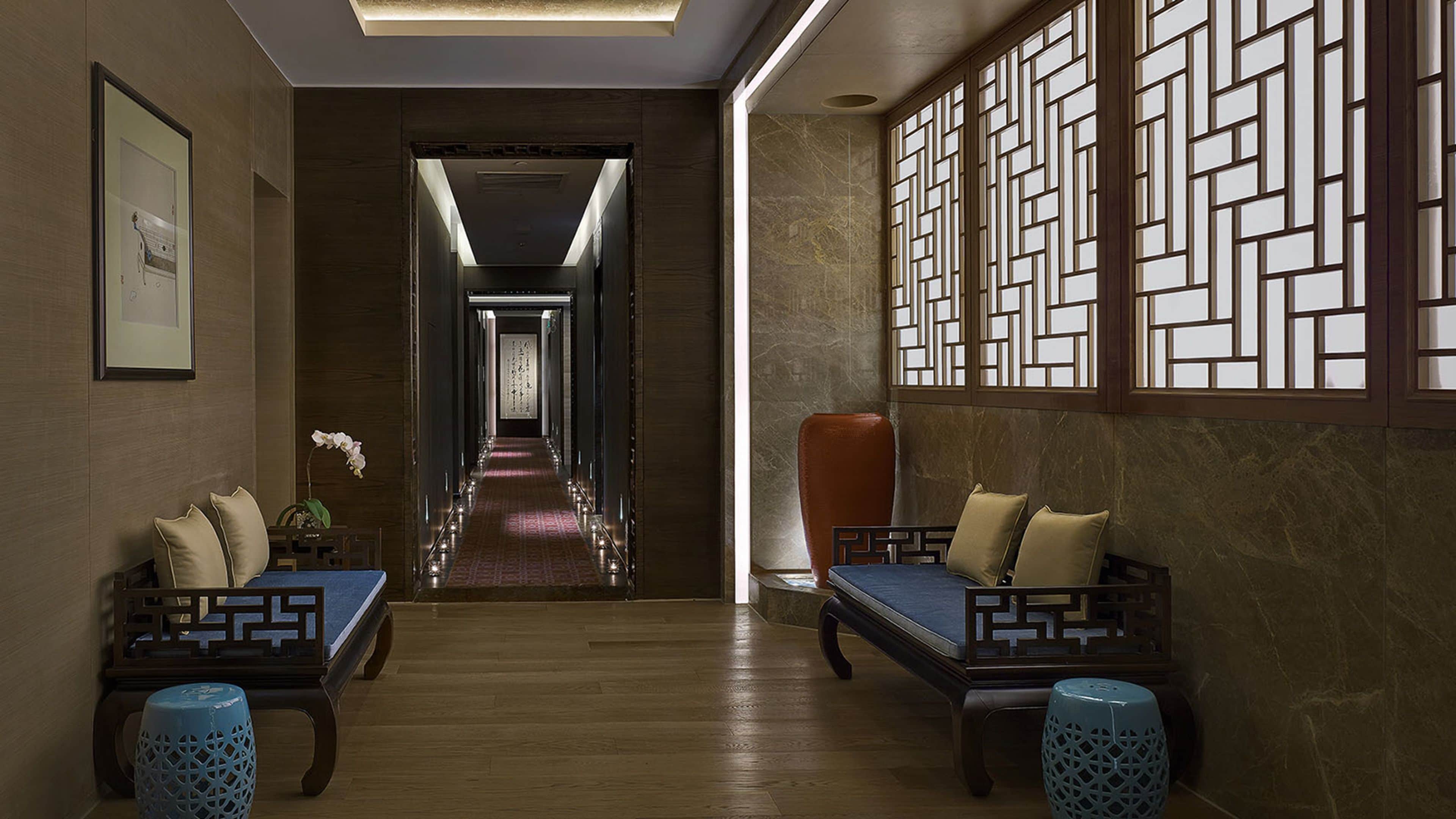 A hallway with a wooden floor, two sofas with cushions, a vase with flowers, and a decorative screen on the right wall.