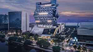 Un moderno edificio de gran altura con un diseño angular distintivo, rodeado por un parque urbano bien cuidado y un río.