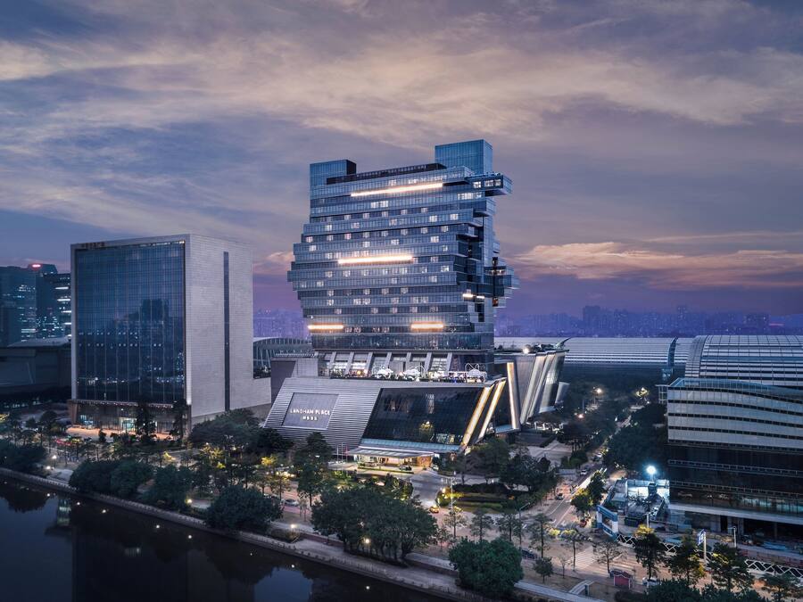 Un moderno edificio de gran altura con un diseño angular distintivo, rodeado por un parque urbano bien cuidado y un río.